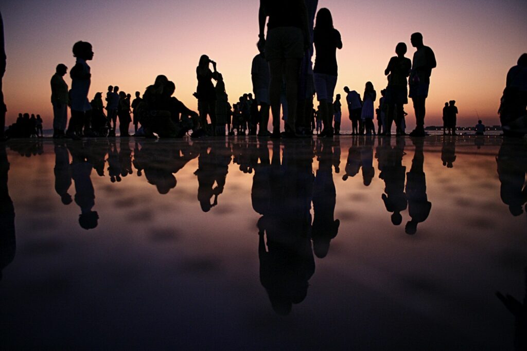 People silhouetted against a sunset sky, reflected in water